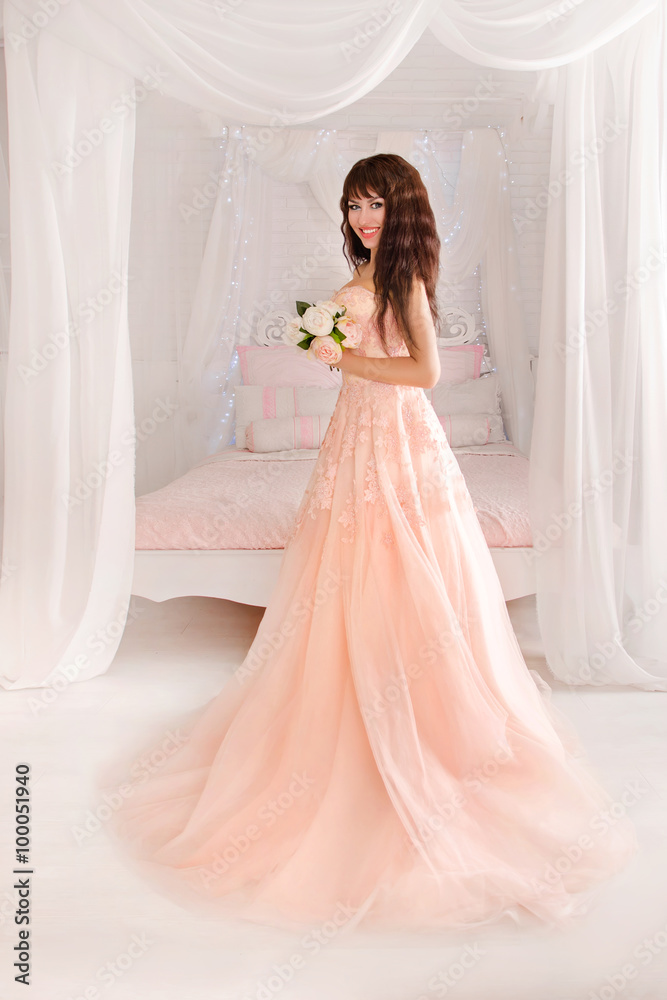 Beautiful young bride in her wedding dress peach, looking down.The gentle light bedroom.Wedding in pink. Beautiful young bride in her wedding dress peach, looking down.The gentle light bedroom.Wedding in pink.