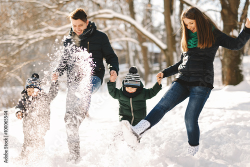 Cute young family with twins and pregnant young mother having fun in winter park on a bright day hugging each other and smiling
