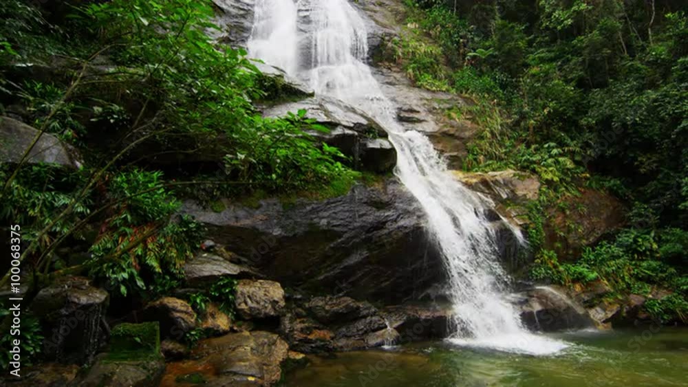 Slow motion shot of a jungle waterfall cascading down a rocky outcropping into a pool of water. Slow motion shot of a jungle waterfall cascading down a rocky outcropping into a pool of water.
