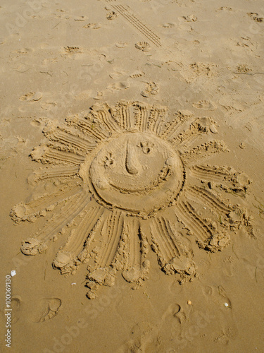 The sign of smiling sun written in sand by fingers on the beach with footsteps around