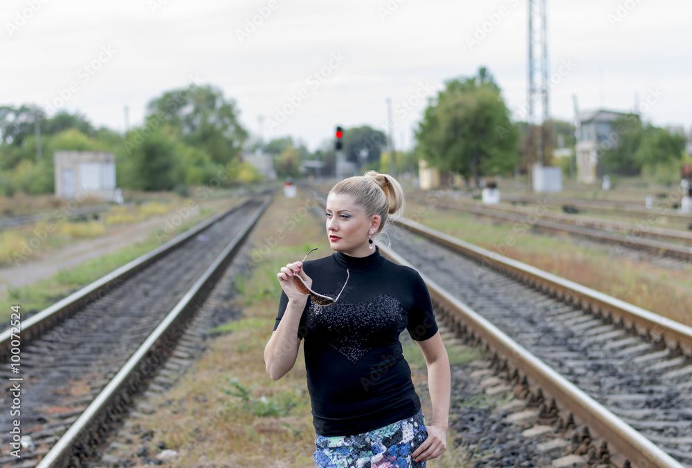 the beautiful woman on railway tracks with sunglasses in hands