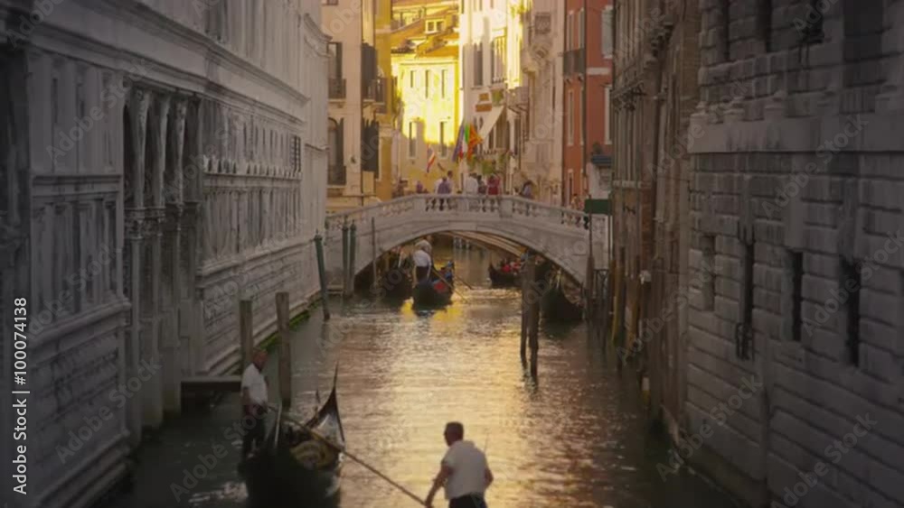 Shot of several gondolas in a canal with a bridge.