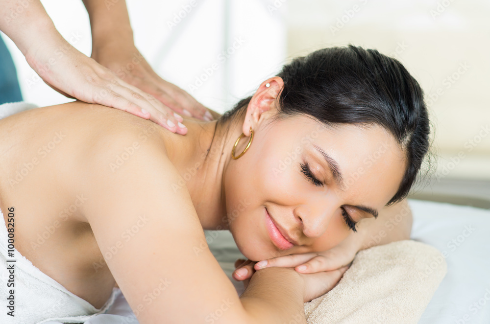 Hispanic brunette model getting massage spa treatment, white towel covering upper body lying horizontal smiling to camera Hispanic brunette model getting massage spa treatment, white towel covering upper body lying horizontal smiling to camera