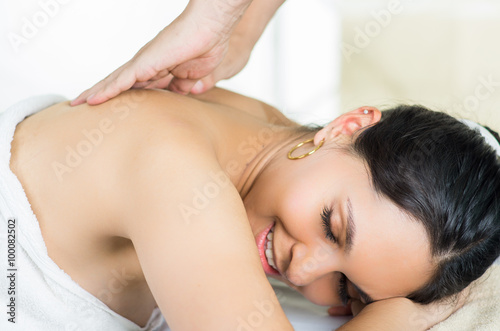 Hispanic brunette model getting massage spa treatment, white towel covering upper body lying horizontal smiling to camera