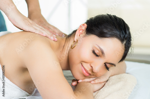 Hispanic brunette model getting massage spa treatment, white towel covering upper body lying horizontal smiling to camera