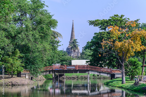 Wooden bridge over canal with Thai temple background.