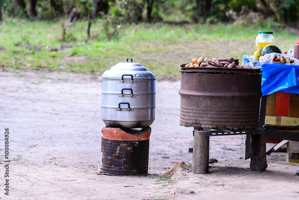 Streaming pot on fire stove and yam grilling on metal grille.