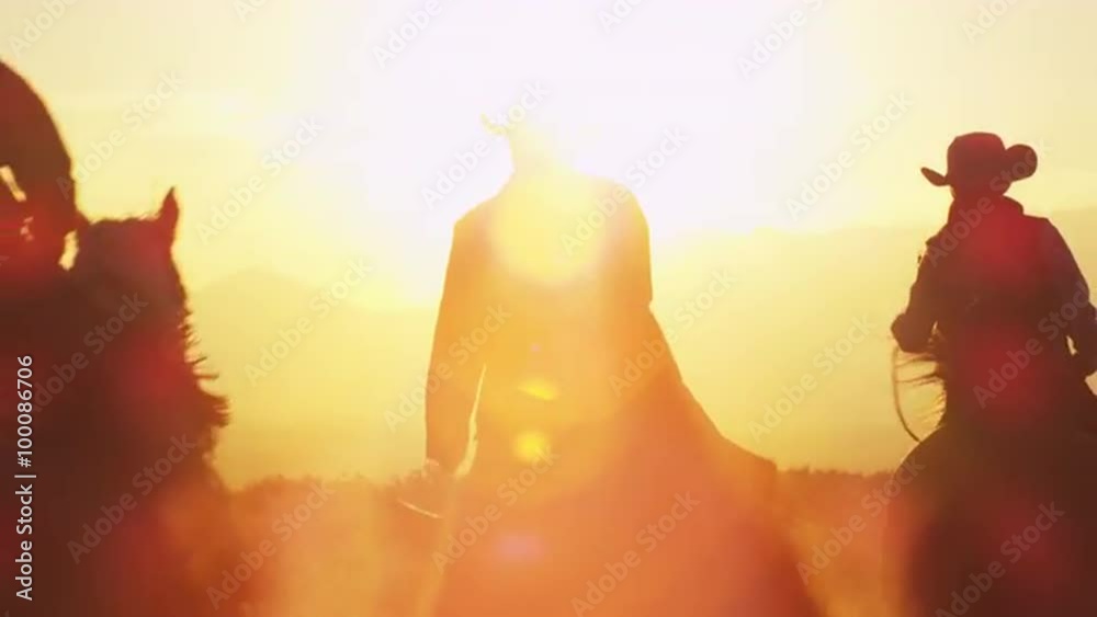 Slow motion Cowboys riding / galloping on horses with lens flare during  golden sunrise / sunset and mountain range..