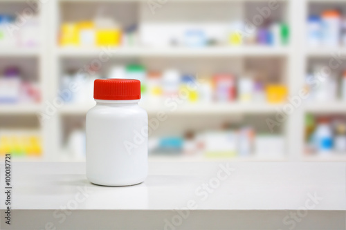 Blank white medicine bottle on counter with blur shelves of drug