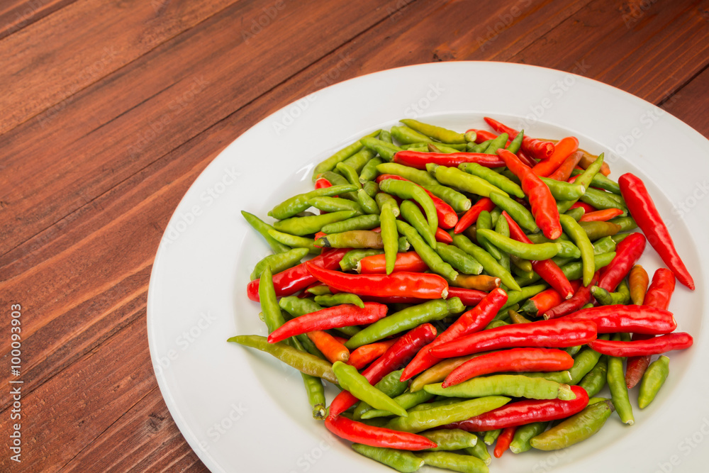 A lot of chili peppers on white dish. Wooden background. A lot of chili peppers on white dish. Wooden background.