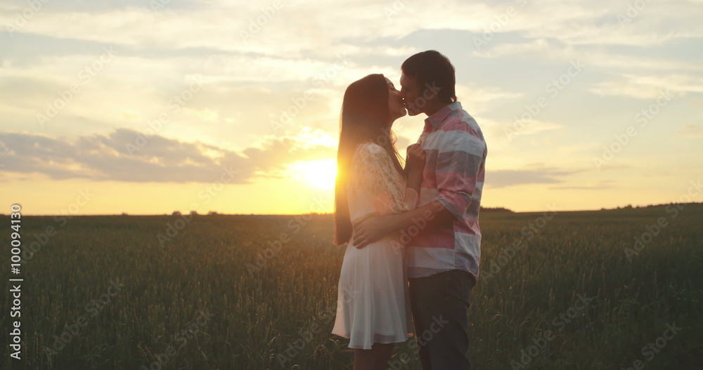 Loving couple hugging and kissing in the meadow at sunset Loving couple hugging and kissing in the meadow at sunset