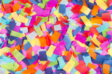 Brightly colored paper confetti background featuring red, yellow, blue, green, orange, and bright pink carnival colors