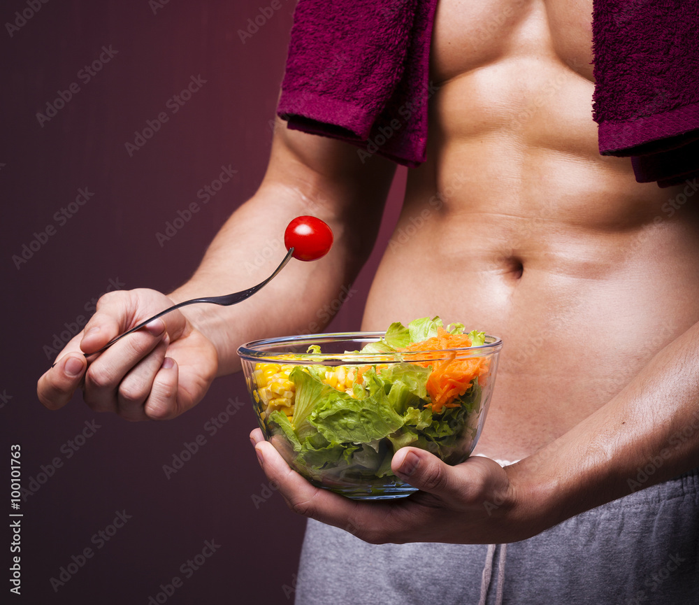 Muscular man holding a bowl of salad on grunge background Muscular man holding a bowl of salad on grunge background
