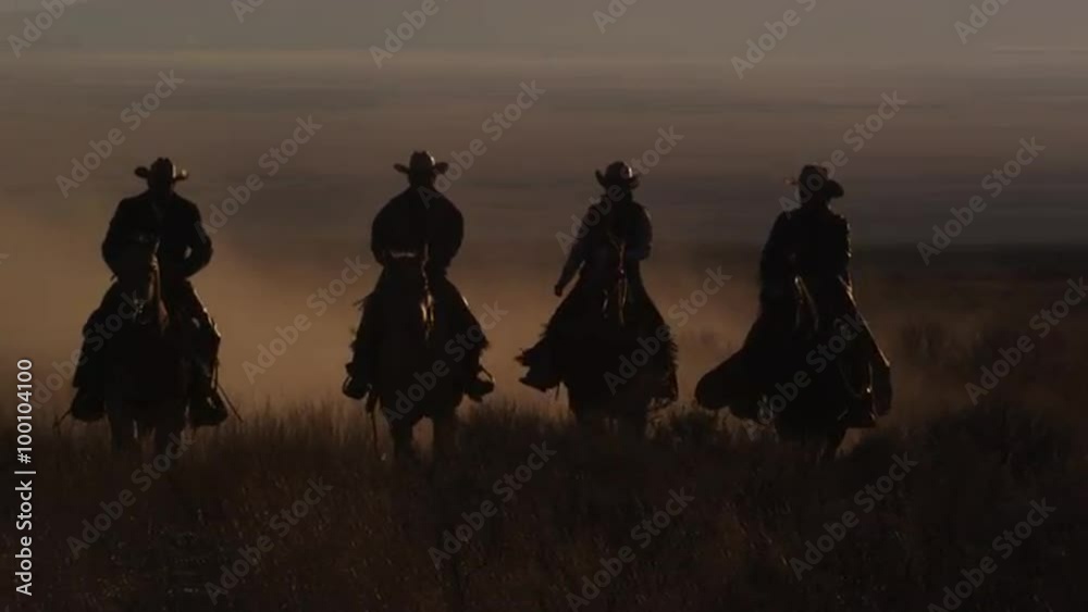  Four western cowboys riding horses at dusk ride past camera, slow motion pan