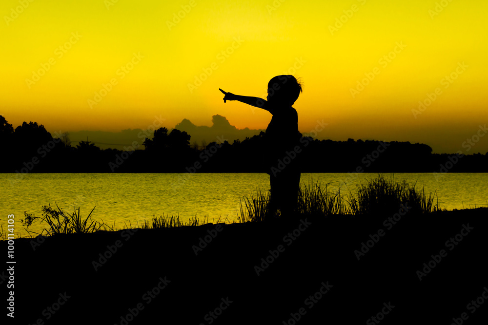 little boy play and point finger at river sunset background