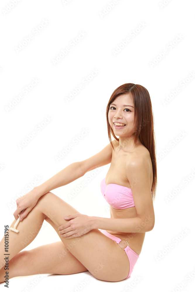 young Japanese woman in a pink bikini shaving legs