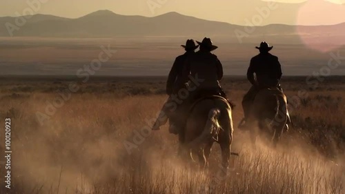 Slow motion shot of Cowboys riding towards distant mountains at dusk with sun flares, golden hour. photo