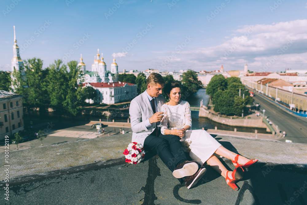 Obraz premium Young couple standing on the roof of the newly-married couple with glasses of champagne in their hands
