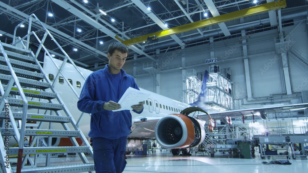 Aircraft maintenance mechanic in blue uniform is going down the stairs while reading papers in a hangar. Shot on RED Cinema Camera.
