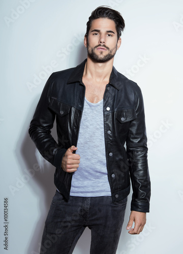 handsome young man posing on grey background with black leather jacket