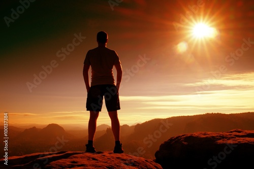 Red filter photo. Slim tourist in pants on the cliff of rock empire is watching down to valley. Hot Sun above.