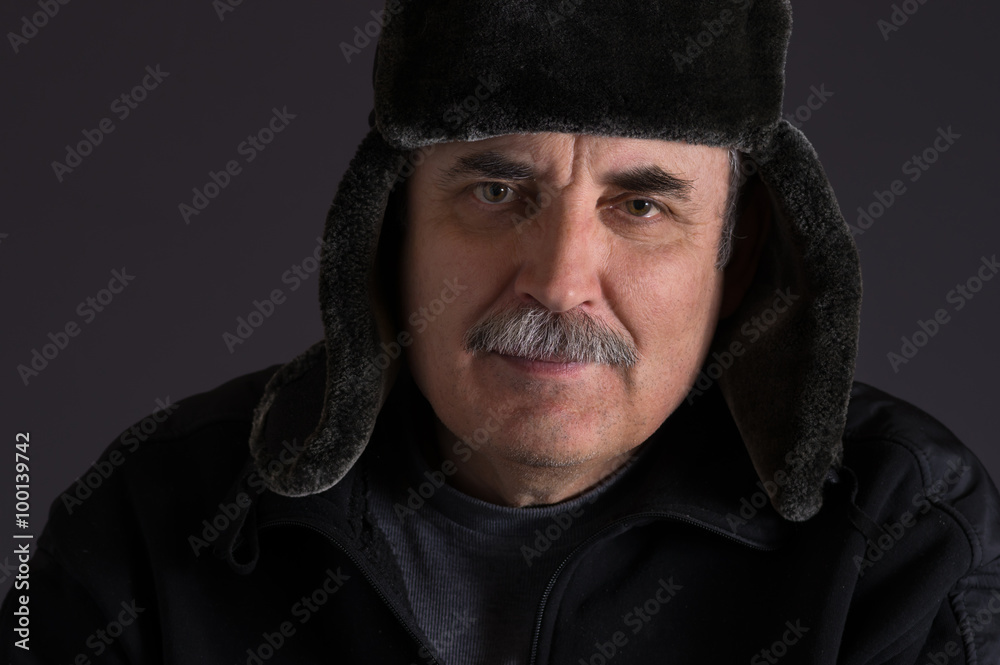 Portrait of mature Caucasian man in fur-cap against dark background Portrait of mature Caucasian man in fur-cap against dark background