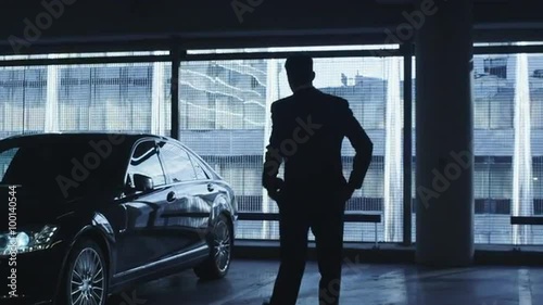 Businessman in a suit is walking towards an executive car in a garage parking lot. Shot on RED Cinema Camera.