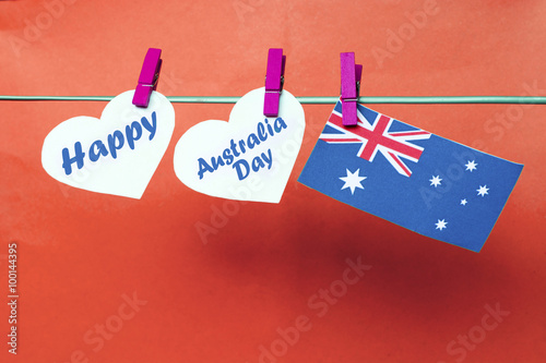 Celebrate Australia Day holiday on January 26 with a Happy message greeting written across white hearts, Australian flag hanging on pegs ( clothespin ) against color background. Toned collage