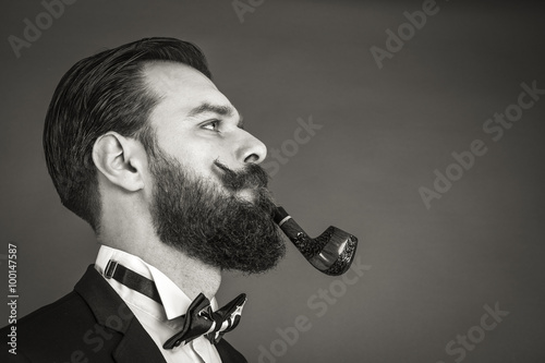 Obraz na płótnie Portrait of a fashionable young man with retro look smoking pipe w salonie