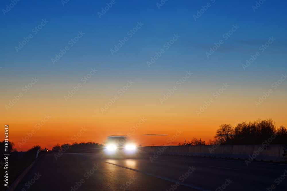 Shining the headlights of a car on the highway after sunset. Blue and orange bright sky at dusk.