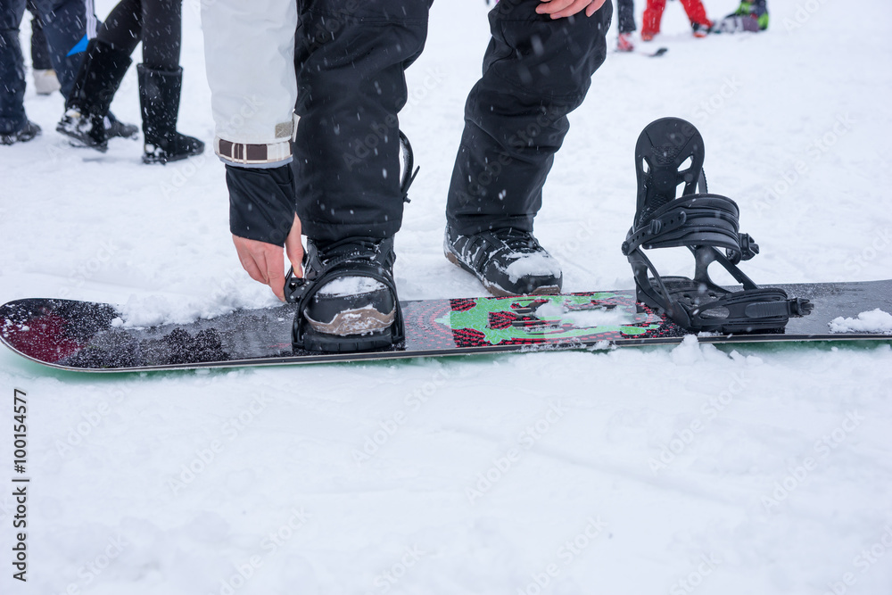 Fototapeta premium Young man tightening the straps on his snowboard