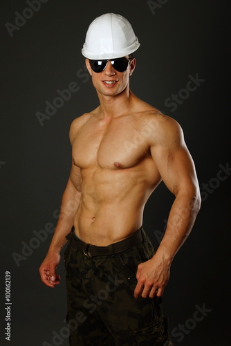 Muscular builder in sunglasses and with a protective helmet on dark background