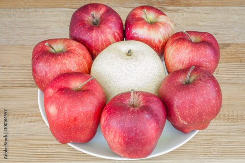 Group of red apple in white dish with chinese pear on wooden background