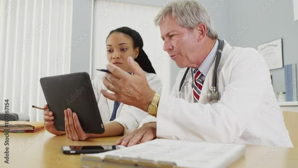 Black and Caucasian doctors working on a tablet in the office Black and Caucasian doctors working on a tablet in the office