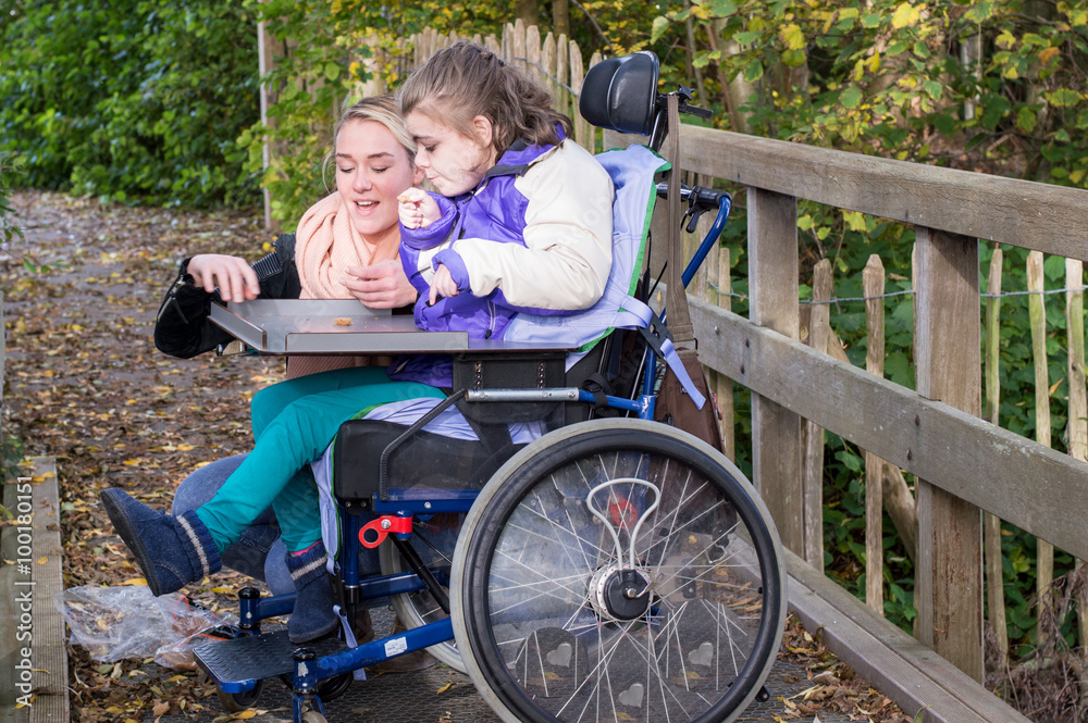 Disability a disabled child relaxing outside / Disability a disabled child in a wheelchair relaxing outside together with a carer Disability a disabled child relaxing outside / Disability a disabled child in a wheelchair relaxing outside together with a carer