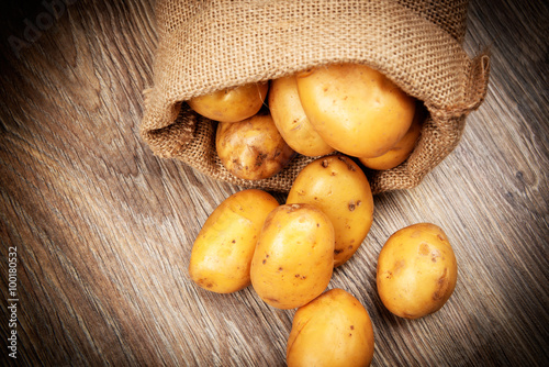 Raw potatoes in the sack on wooden background