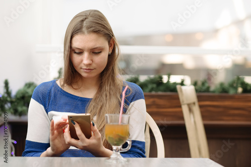 Woman using her cellphone with touchscreen in light cafe