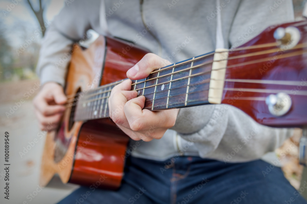 Fototapeta premium Young man playing acoustic guitar close up outdoors in autumn park