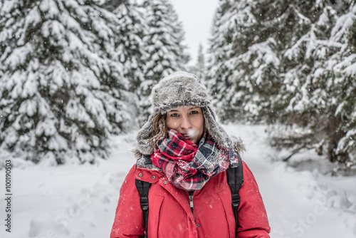 Outdoor portrait of young woman, looking at the camera. Snow covered pine trees on the background. 