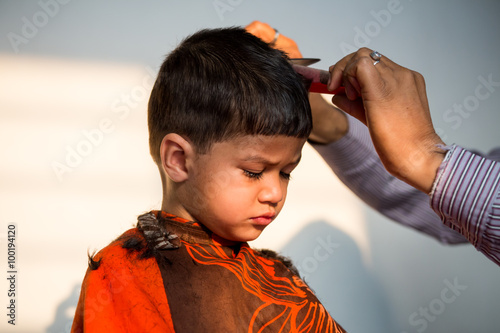 two year old kid having a haircut with wet eyes after crying early morning with golden light falling on his face