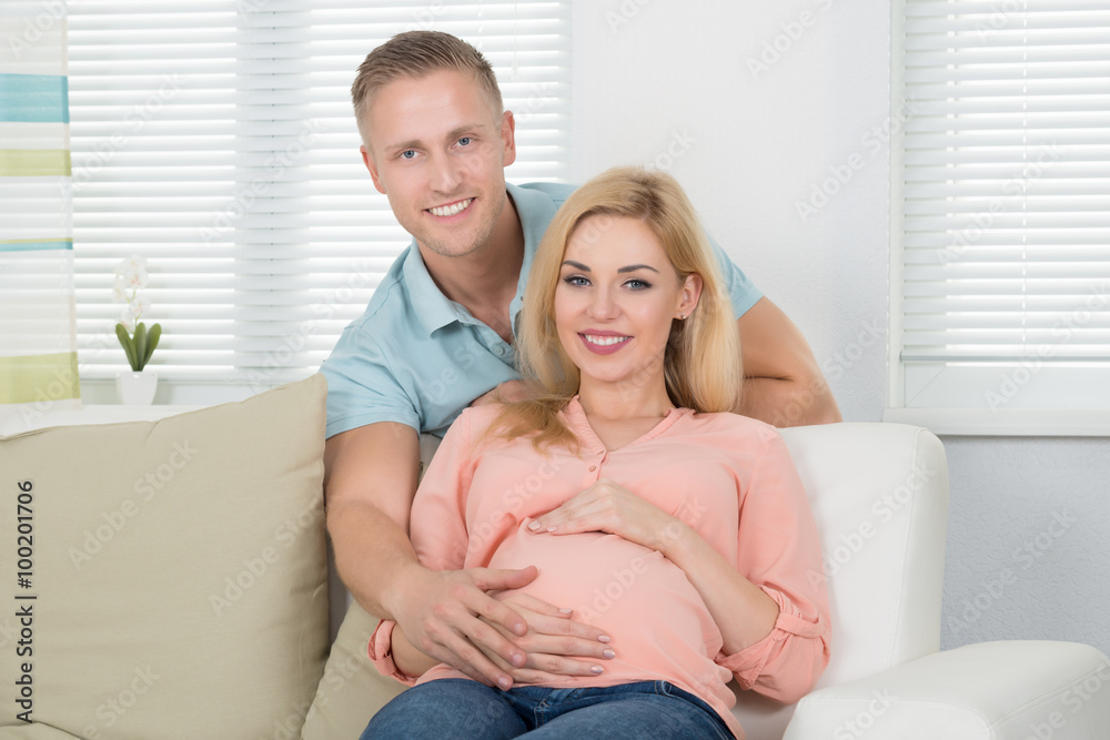 Happy Expecting Couple Sitting On Sofa At Home Happy Expecting Couple Sitting On Sofa At Home