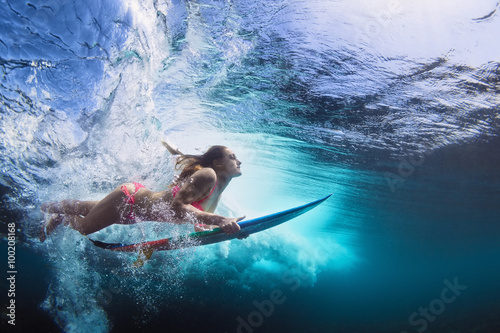 Young girl in bikini - surfer with surf board dive underwater with fun under big ocean wave. Family lifestyle, people water sport lessons and beach swimming activity on summer vacation with child