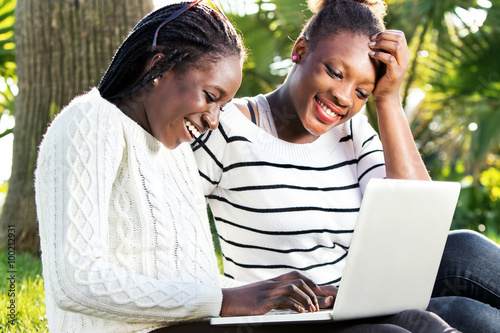 African teen girls having fun on laptop in park. © karelnoppe