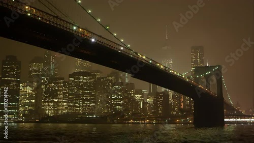 High speed static zoomed view at night overlooking the East River and the Brooklyn Bridge.