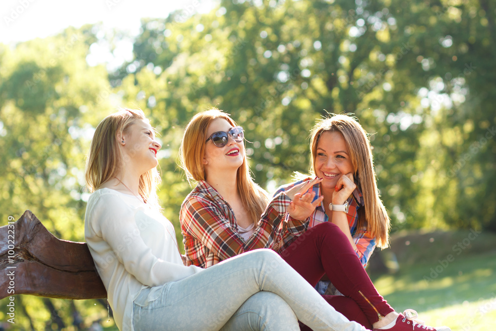 Three friends sitting on a park bench, chatting and enjoying the sunny day Three friends sitting on a park bench, chatting and enjoying the sunny day