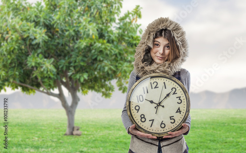 portrait of a pretty young woman wearing a hood and holding a big clock