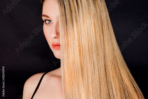 Beautiful young blonde woman with long straight hair on a dark background