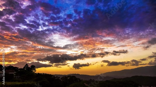 Very colorful day to night time lapse of clouds at sunset in the tropic. The sun flashes all around during the setting and city lights showoff at night