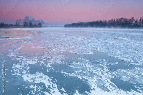 Smoking chimneys over a misty and freezing river during dusk