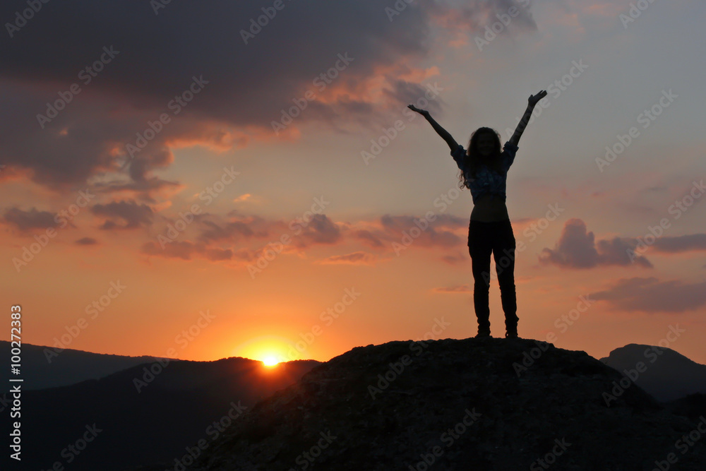 Silhouette of a girl standing on a mountain with his hands up ag